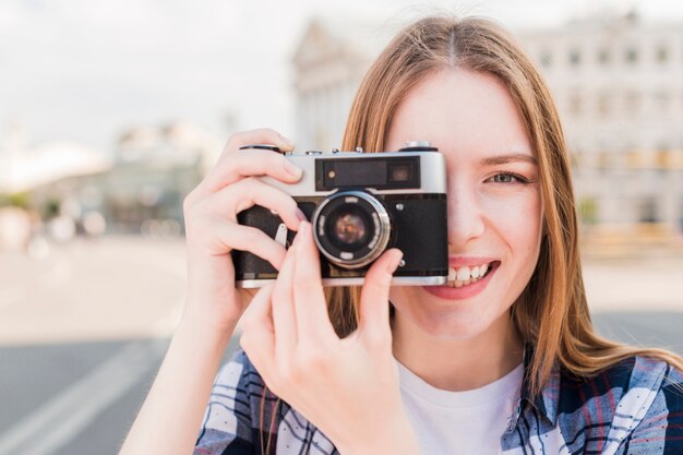 屋外でカメラで写真を撮る若い女性の笑みを浮かべてください。