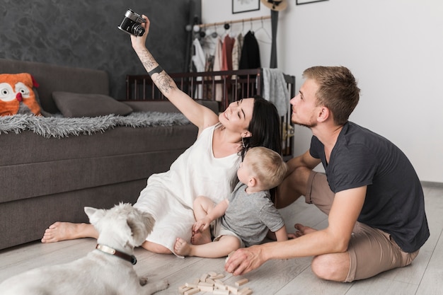 Smiling young woman taking selfie of her family while sitting in the living room