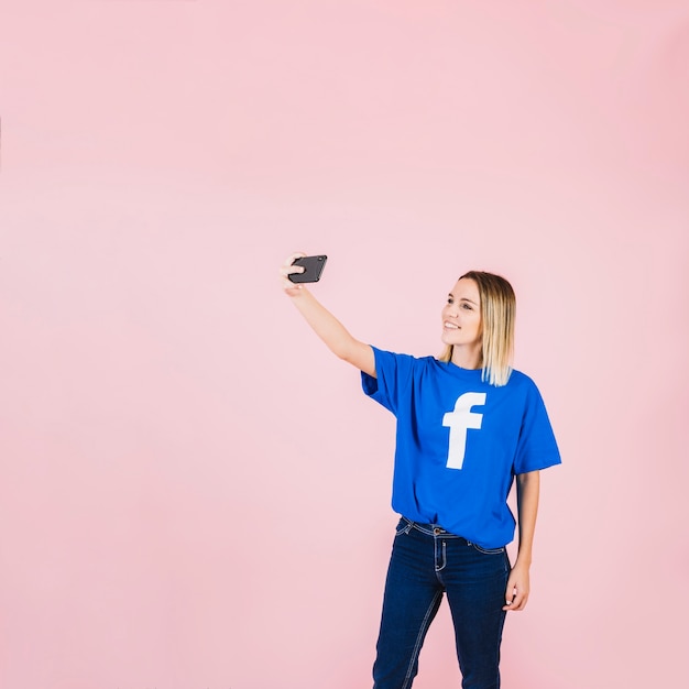 Free photo smiling young woman taking selfie with cellphone