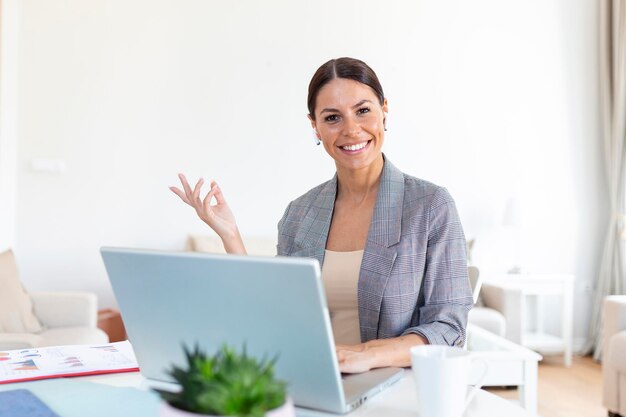 Улыбающаяся молодая женщина, использующая ноутбук дома, смотрит на экран в чате в беспроводной гарнитуре, проводя видеоконференцию с бизнес-тренером, обучающим с помощью веб-камеры