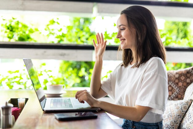 Smiling young woman using laptop and making video call in cafe.