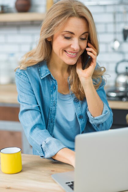 スマートフォンで話しているラップトップを使用して笑顔の若い女性