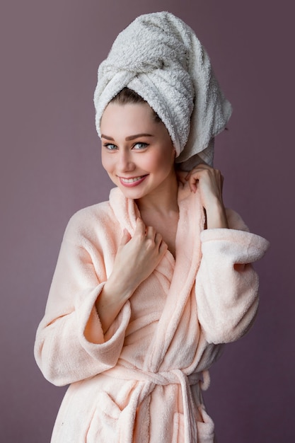 Free photo smiling young woman wearing bathrobe and towel on her head standing on pink purple.