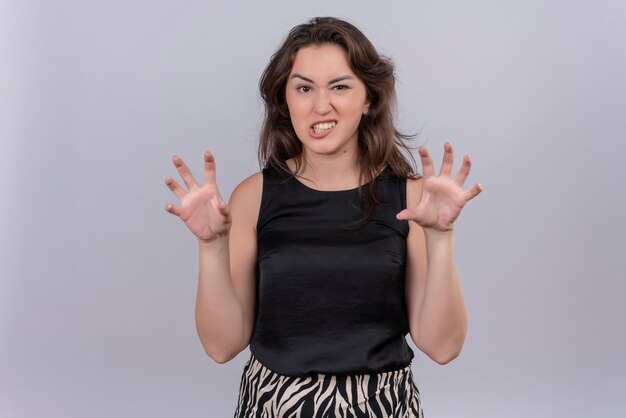 Smiling young woman wearing black undershirt showing tiger gesture on white wall