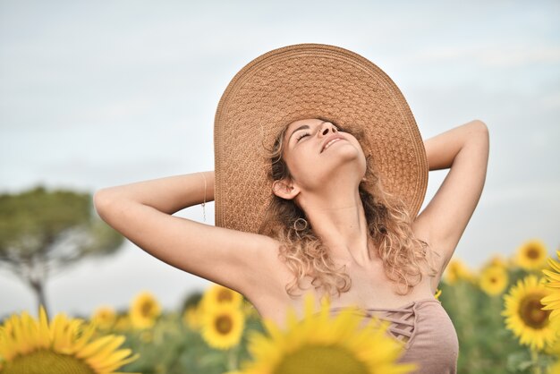 Sorridente giovane donna che indossa un cappello nel campo di girasole - il concetto di felicità