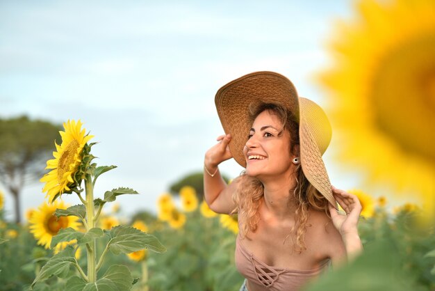 ひまわり畑で帽子をかぶって笑顔の若い女性