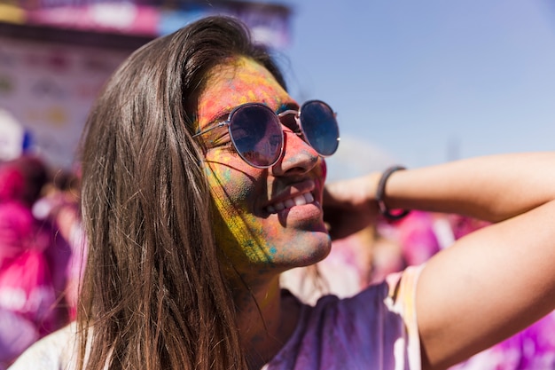Foto gratuita occhiali da sole d'uso sorridenti della giovane donna coperti di colori di holi