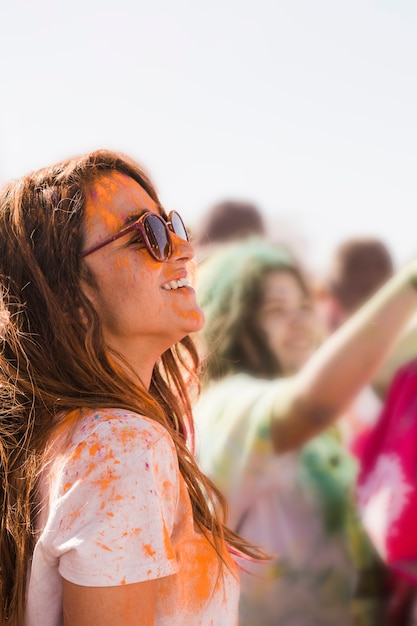 Smiling young woman wearing sunglasses mess with an orange holi powder