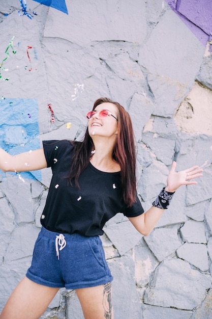 Smiling young woman wearing sunglasses posing in front of painted stone wall