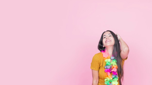Smiling young woman with colorful fake garland standing against pink background
