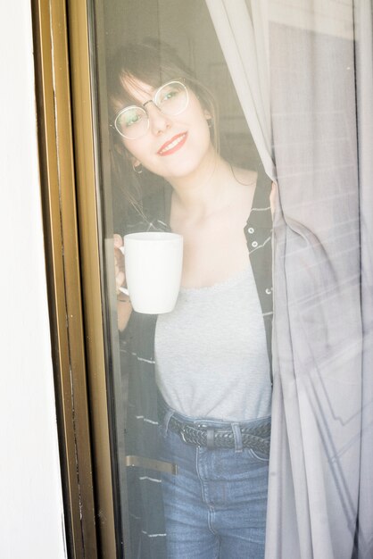 창문을 통해보고 커피 한잔과 함께 웃는 젊은 여자