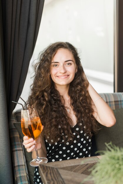 Улыбается молодая женщина с фигурные длинные волосы, проведение стакан напитка