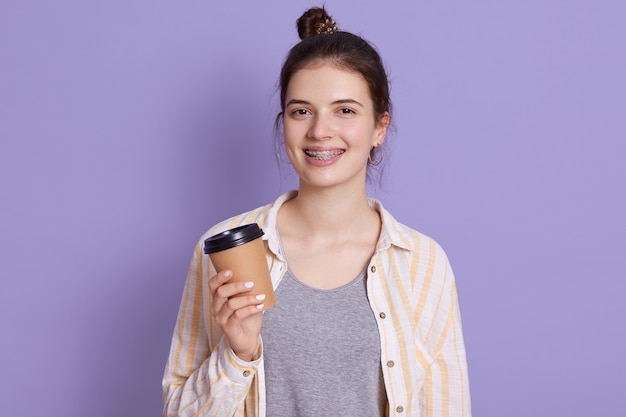 Smiling young woman with hair bun holding take away coffee in hands