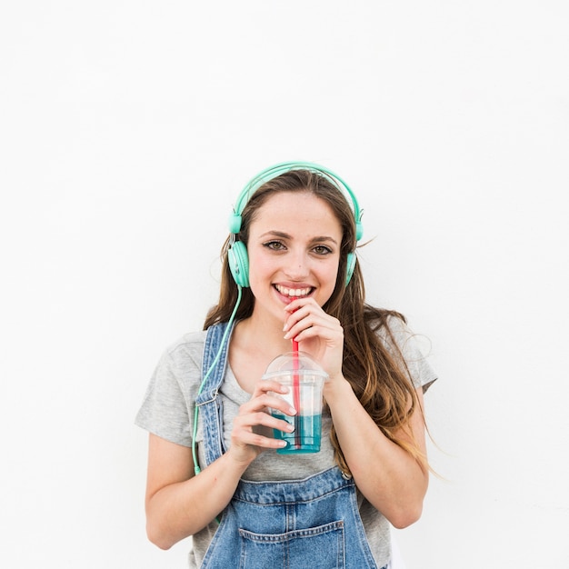 Smiling young woman with headphone on his head drinking juice