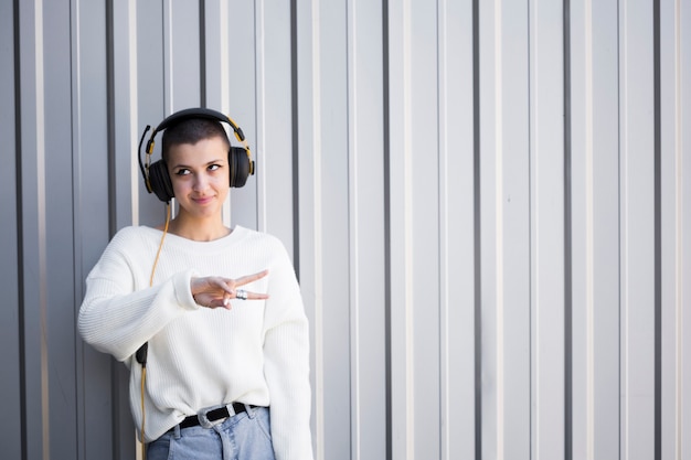 Smiling young woman with headphones and bob hairstyle gesturing peace sign