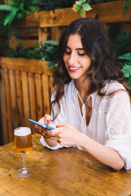 Улыбается молодая женщина со смартфоном и пивом