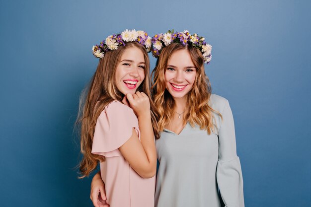 Smiling young woman in wreath embracing her sister on blue wall