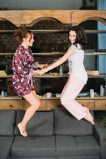 Free photo smiling young women jumping on sofa