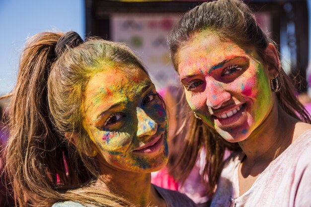 카메라를보고 그들의 얼굴에 holi 색상으로 젊은 여성 미소