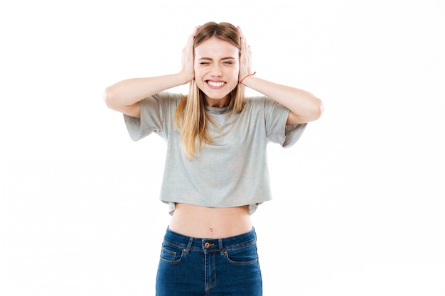 Smiling young young woman standing and covering her ears with hands