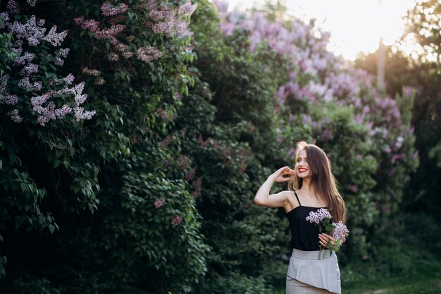 The smilling girl stands near bushes with flowers