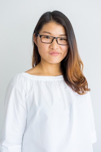 Smirking young Chinese woman in eyeglasses looking at camera. 