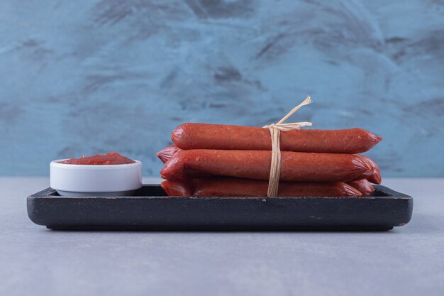 Smoked sausages and ketchup on dark plate. 