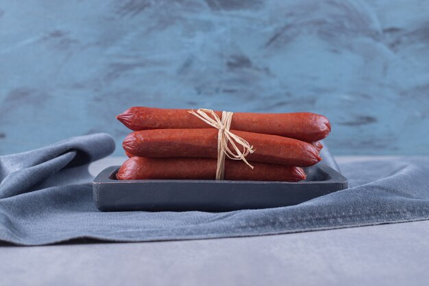 Smoked sausages tied with rope on dark board. 