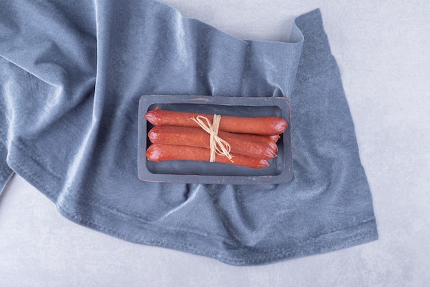 Smoked sausages tied with rope on dark board. 