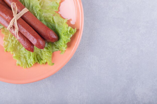 Smoked sausages tied with rope on orange plate. 