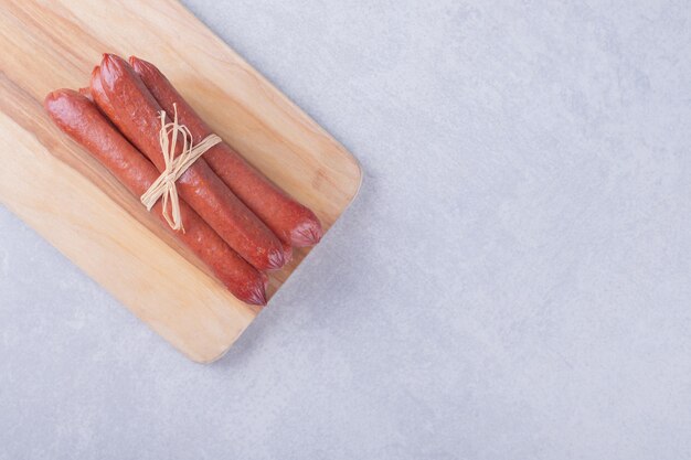 Smoked sausages tied with rope on wooden board. 