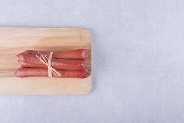 Smoked sausages tied with rope on wooden board. 