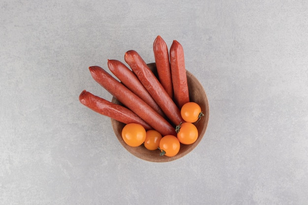 Smoked sausages and tomatoes in wooden bowl.