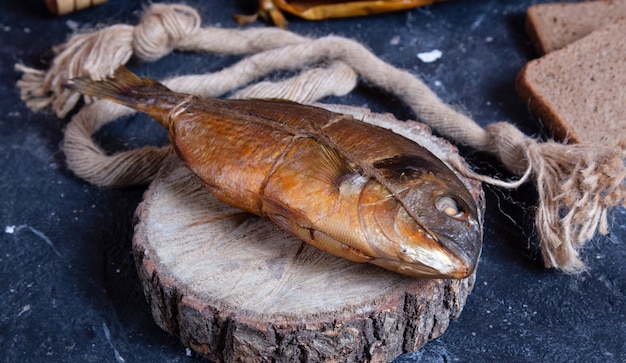 Smoked whole dry fish on a piece of wood. Rustic thread around