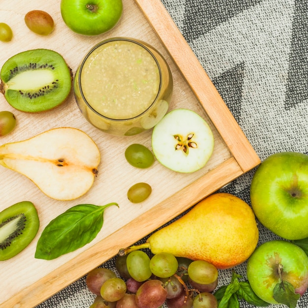 Free photo smoothie glass and fresh fruits on wooden tray and over tablecloth