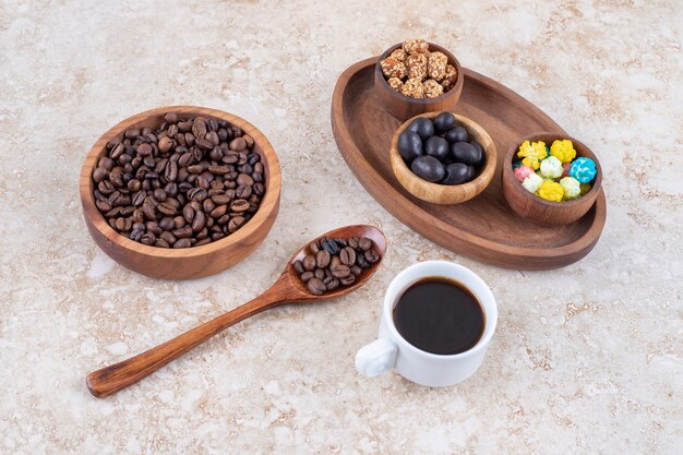 Snack assortment in a wooden tray next to coffee beans and a cup of brewed coffee 