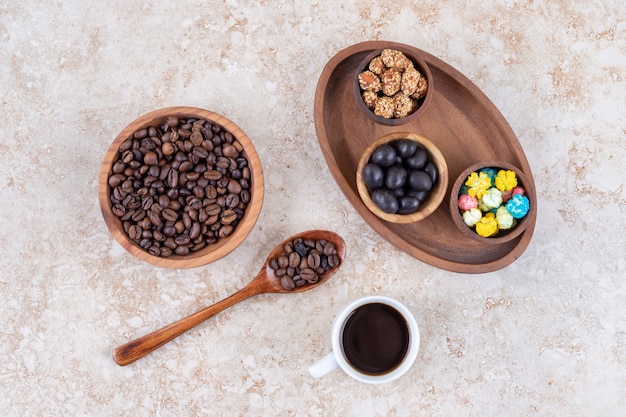 Snack assortment in a wooden tray next to coffee beans and a cup of brewed coffee 