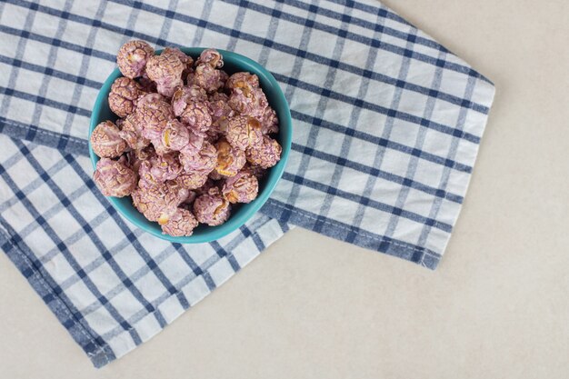 Snack bowl resting on a folded towel and filled with candy coated popcorn on marble.