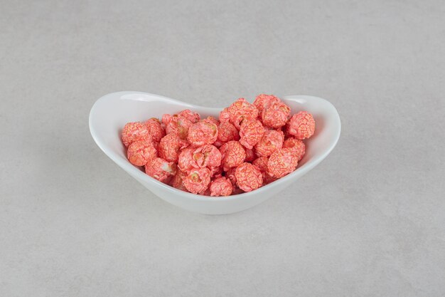 Snack serving of red popcorn candy in an oval bowl on marble table.