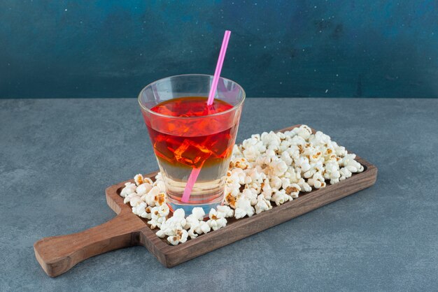 Закуска набор кучи попкорна и стакан холодного сока подается на деревянной доске на синем фоне. Фото высокого качества