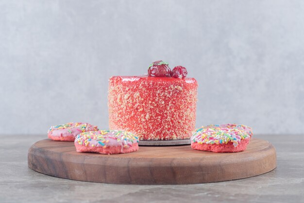 Snack-size donuts around a cake topped with strawberry syrup on a board on marble surface