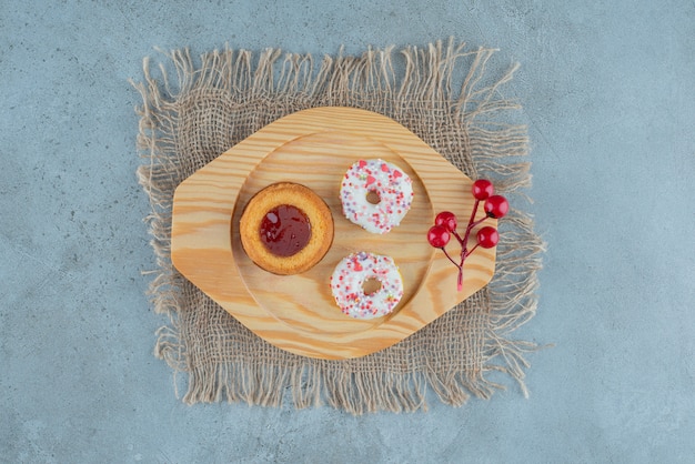 Snack-size donuts and a jelly-filled cake on a wooden platter on marble background. High quality photo