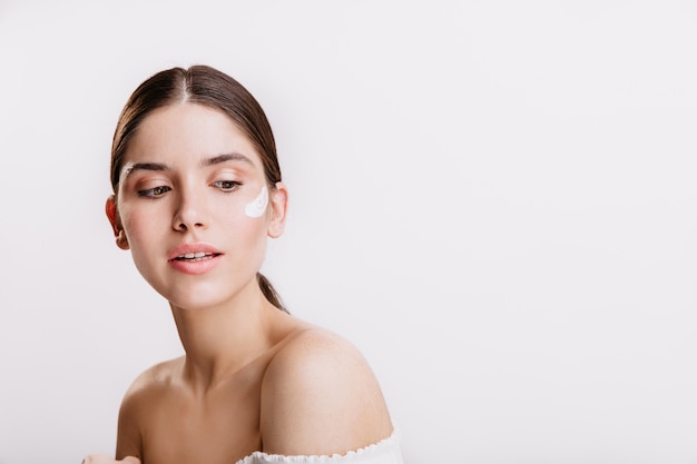 Snapshot of beautiful dark-haired woman with nourishing cream on her face.