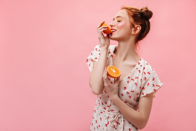 Snapshot of charming girl dressed in dress with cherry print Woman with yellow eyeshadows holds oranges and looks into camera