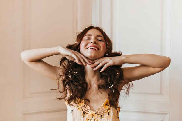 黄色の市松模様のトップポーズで女性を楽しんで笑ってカールで花と満足している女の子のスナップショット