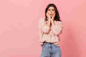 Free photo snapshot of dolorous dark-haired girl in pink studio. woman in knitted sweater sadly looks into camera.