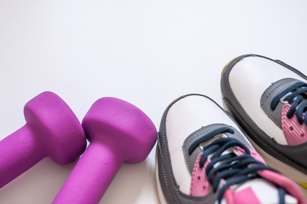 Sneakers and dumbbells fitness on a white background. Different tools for sport. Concept healthy lifestyle, sport and diet. Sport equipment. Copy space. Flat lay of fitness and workout accessories