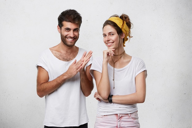 Free photo sneaky sly and scheming young european man and woman dressed in stylish clothing looking with mysterious smiles, male making gesture as if washing his hands