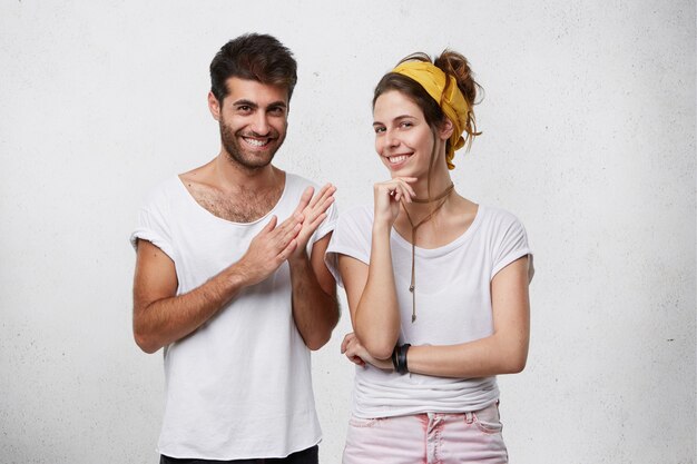 sneaky sly and scheming young European man and woman dressed in stylish clothing looking with mysterious smiles, male making gesture as if washing his hands