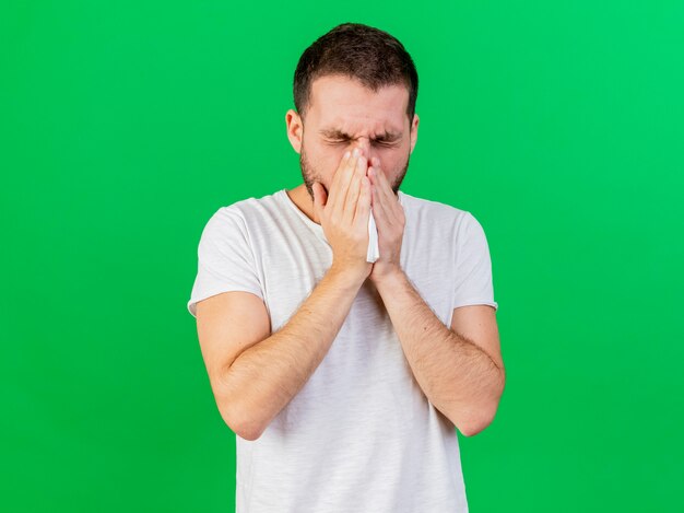 Sneezng young ill man grabbed nose isolated on green background